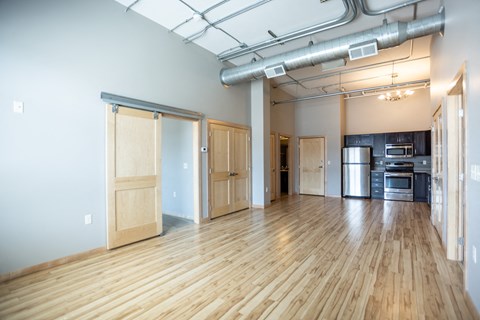 an empty living room with wood floors and a kitchen