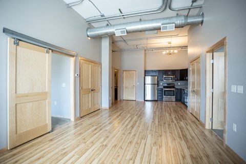 an empty living room with wood floors and a kitchen