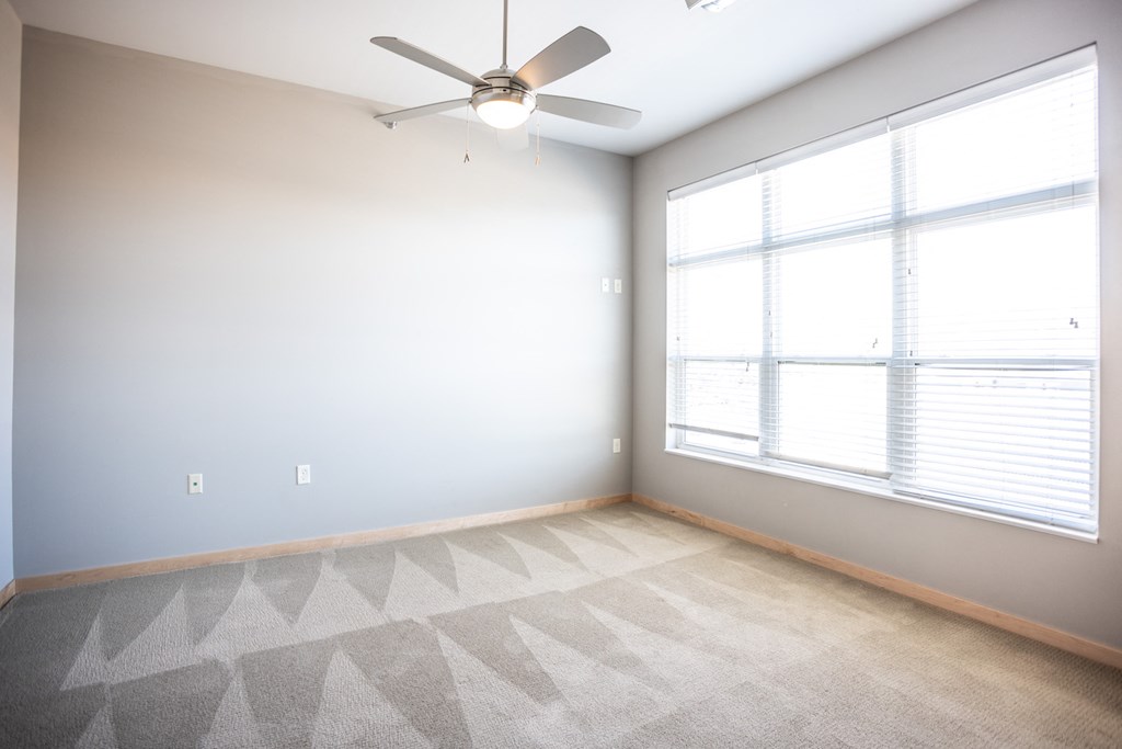 an empty room with a ceiling fan and two windows