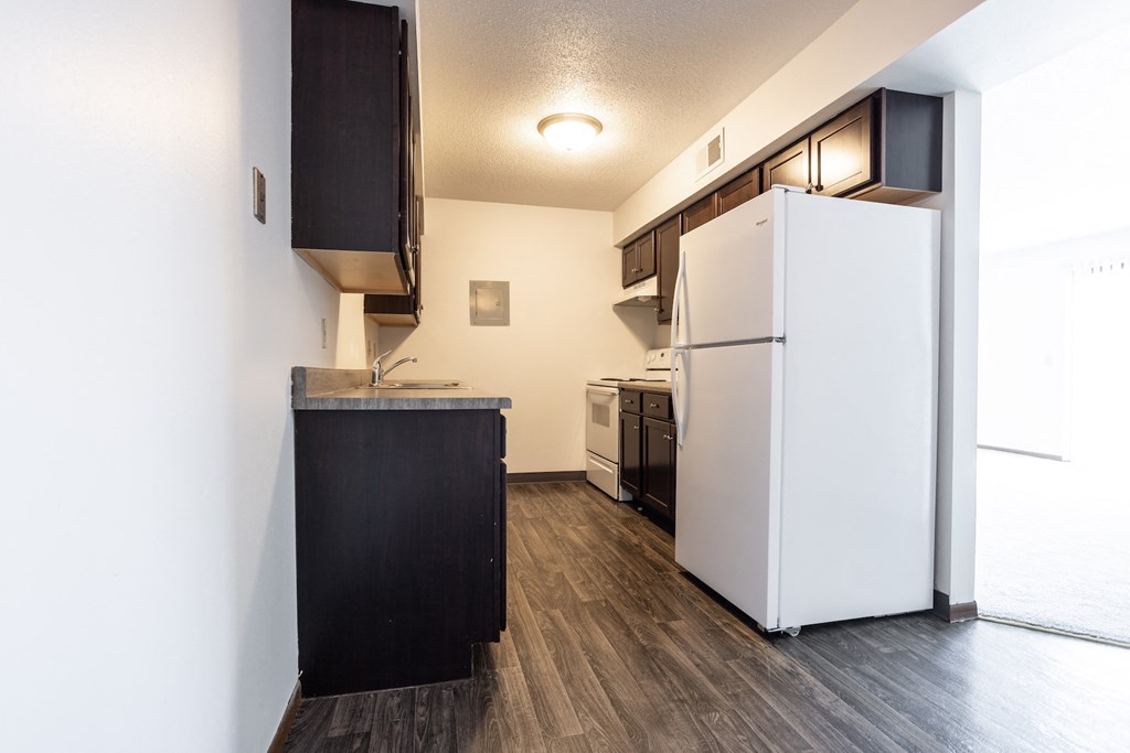 an empty kitchen with a white refrigerator and a black counter top