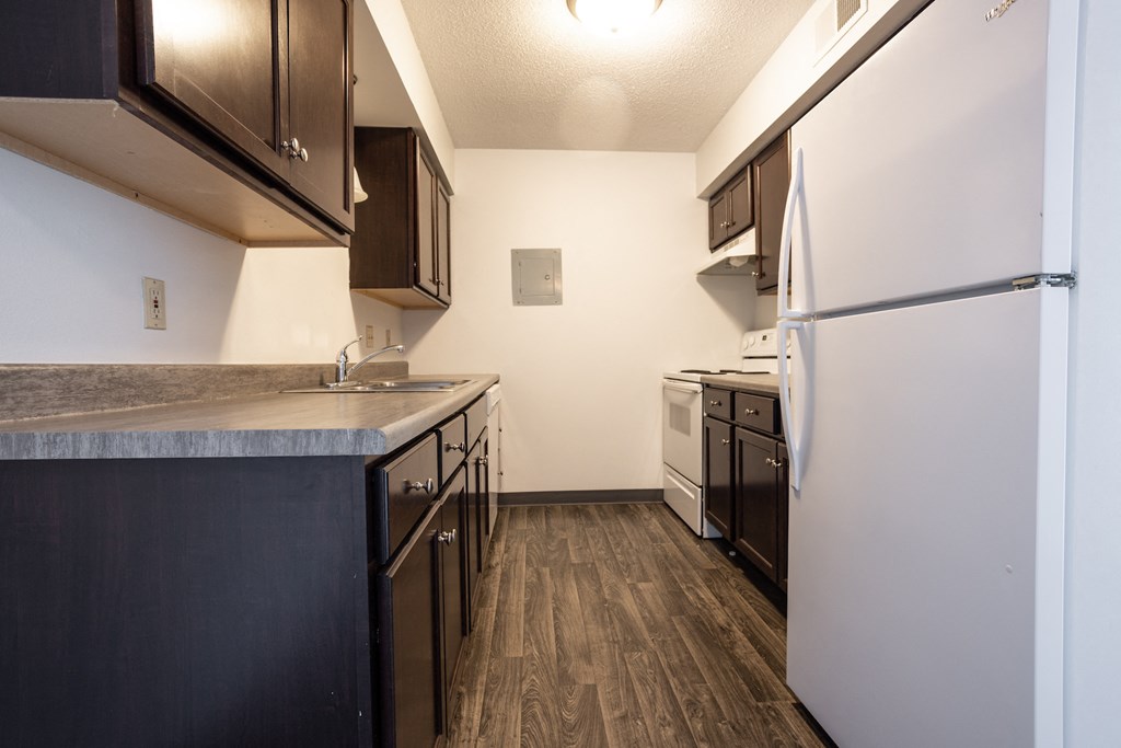 an empty kitchen with white appliances and wood flooring and a refrigerator