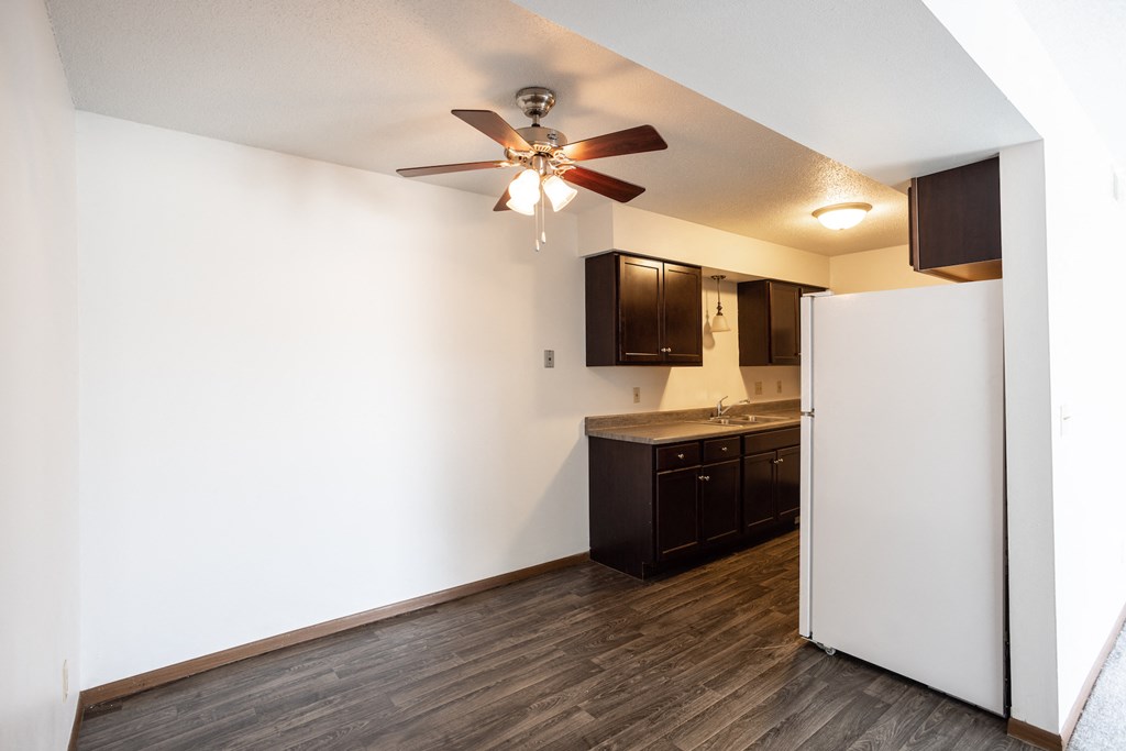 an empty living room with a ceiling fan and a kitchen