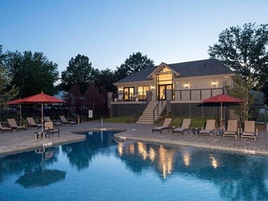 Swimming pool surrounded by lounge chairs with the Yardley Crossing clubhouse in the back at dusk