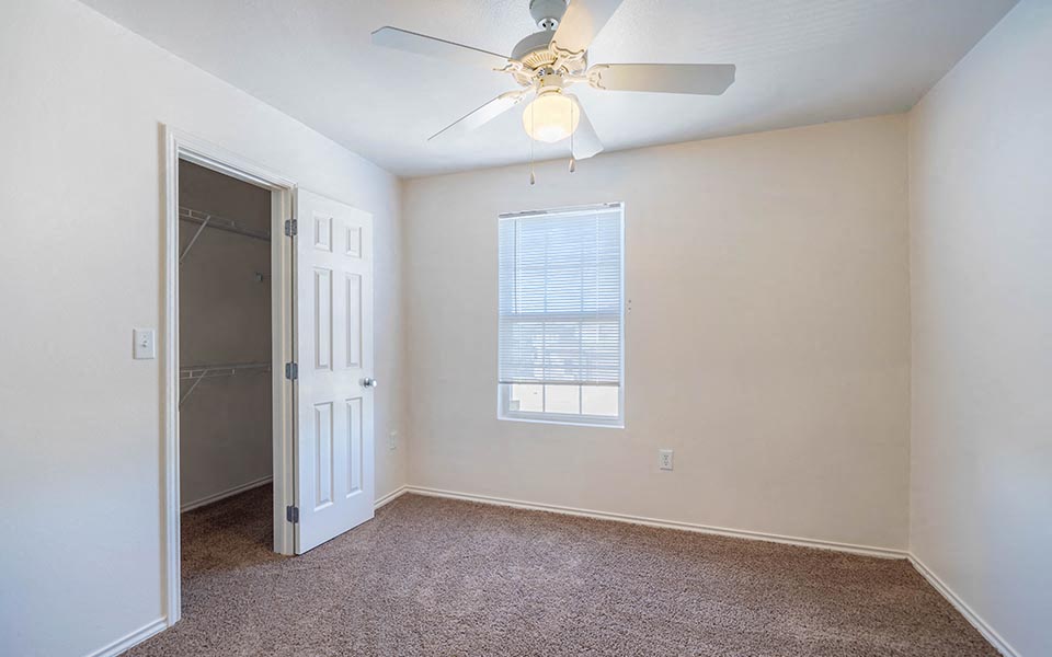 an empty bedroom with a ceiling fan and a closet