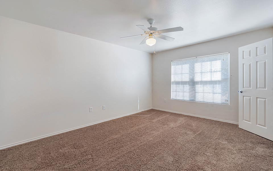 an empty bedroom with a ceiling fan and a window