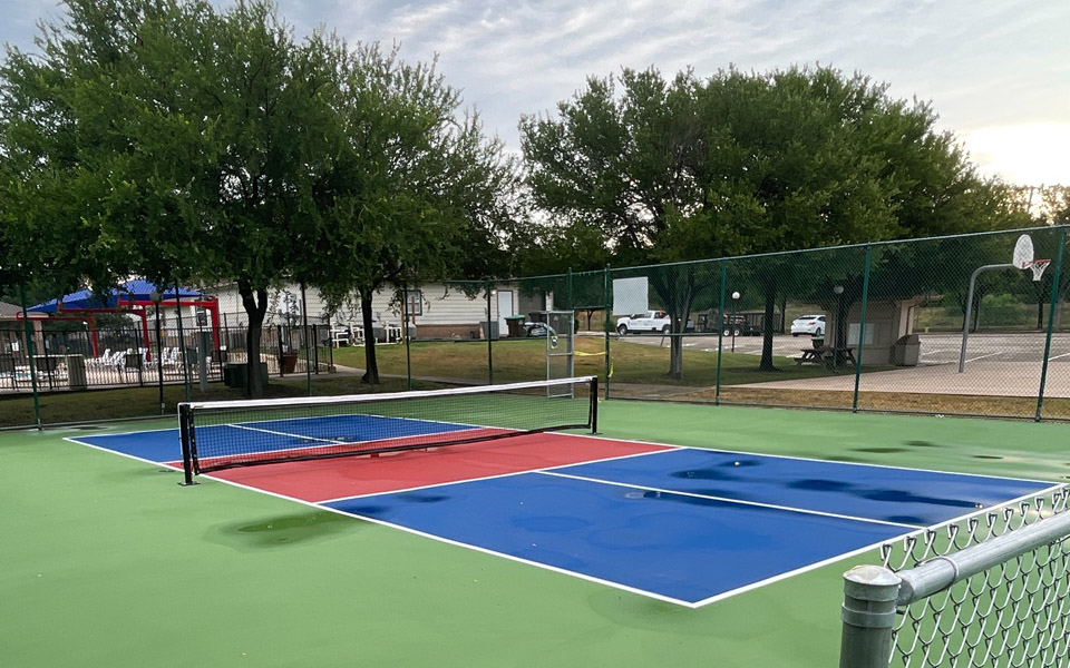A blue and red tennis court with a green fence surrounding it.