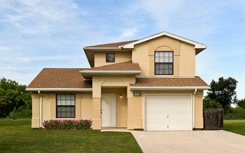 a tan house with a garage and a lawn