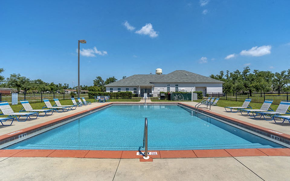 a swimming pool with chairs and a house in the background
