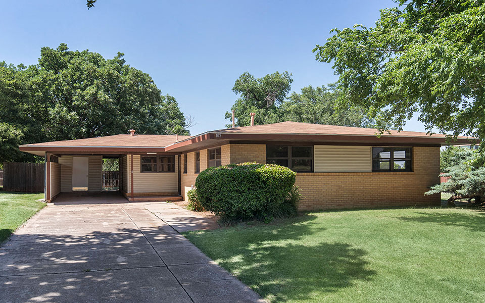 a brown brick house with a driveway and lawn