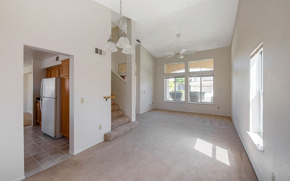 an empty living room with a refrigerator and a staircase