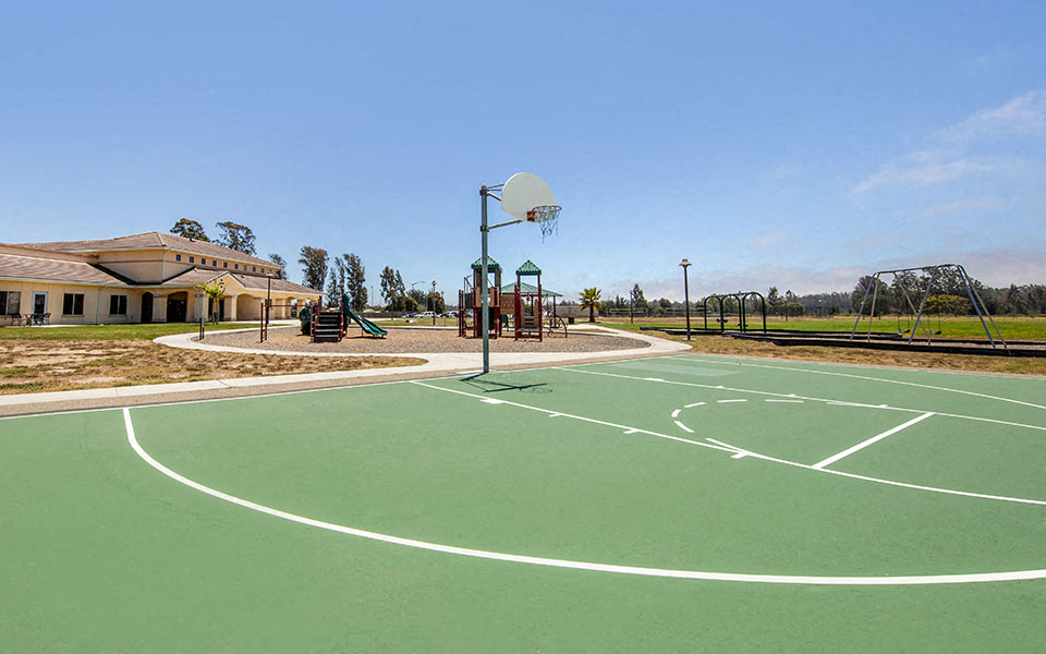a basketball court with a playground and building in the background