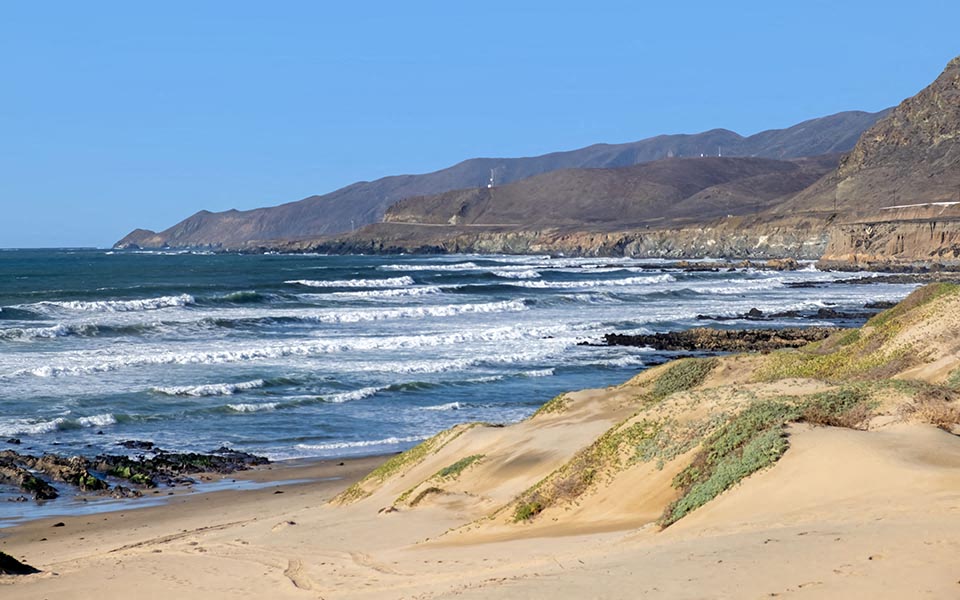 a beach with the ocean and mountains in the background