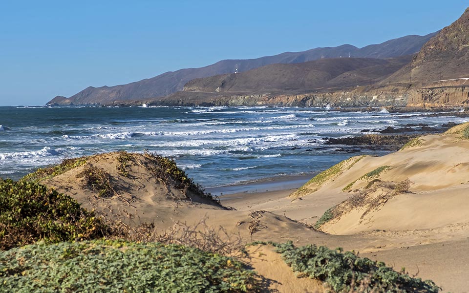 a beach with waves and mountains in the background
