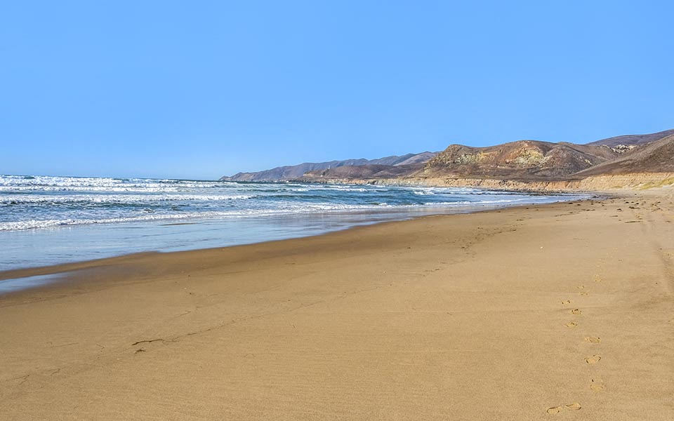 a sandy beach with the ocean and mountains in the background