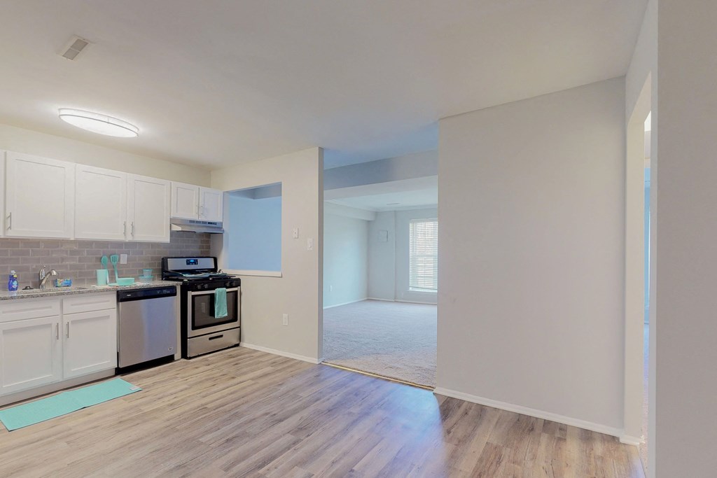 an empty kitchen and living room with a hard wood floor and white cabinets