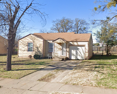 a small tan house with a driveway and a tree