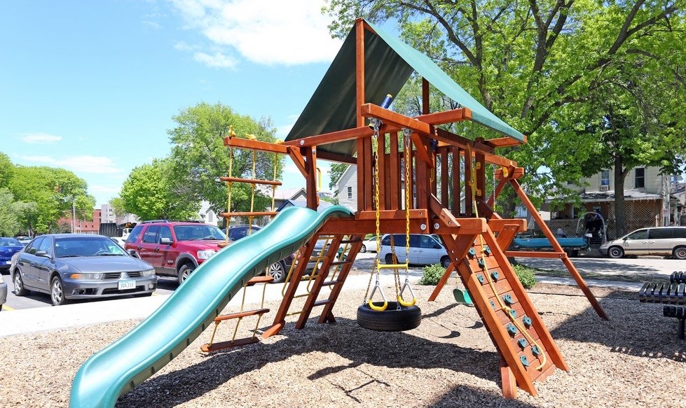 A playground with a green slide and a red car parked in the background.