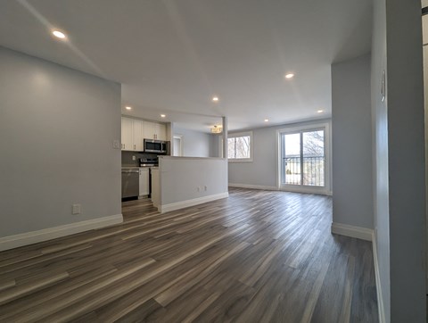 A spacious room with wooden flooring and a kitchen area in the background.