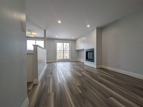 A spacious room with wood flooring and a large window.