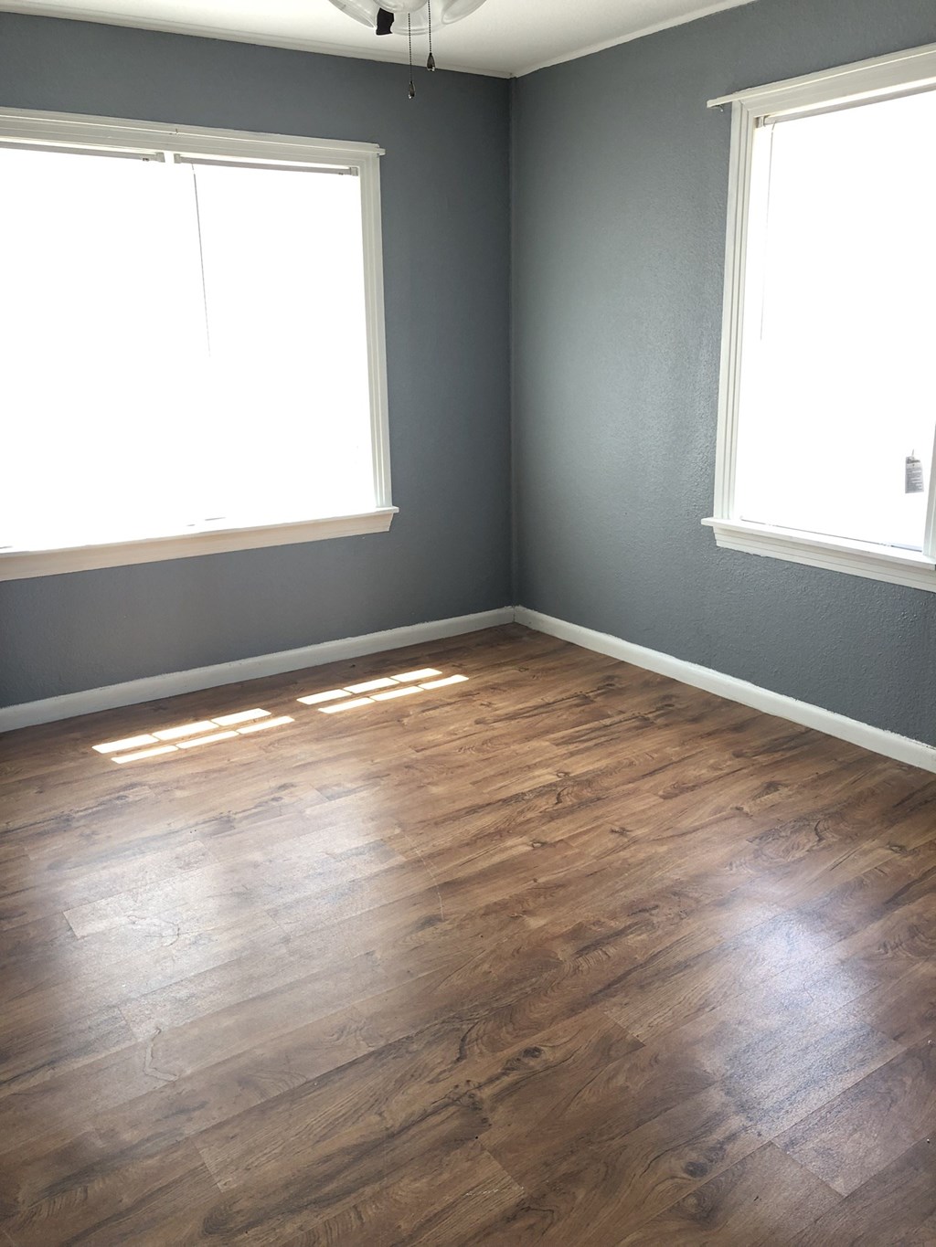 an empty room with wood floors and two windows
