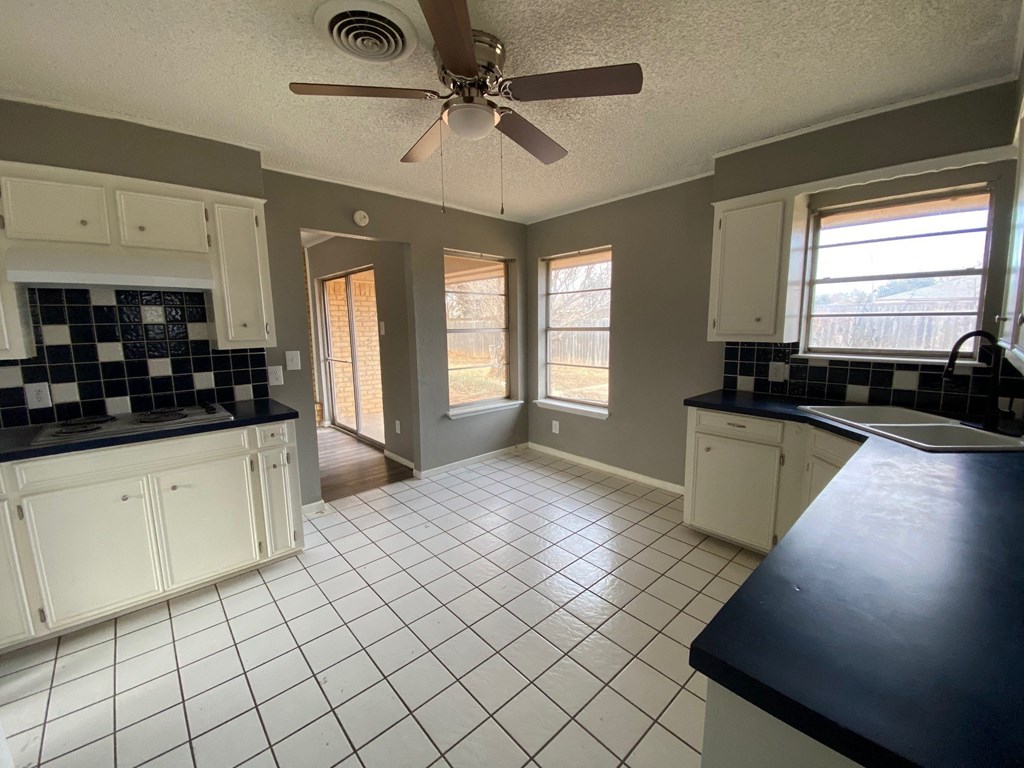 an empty kitchen with white tiles and a ceiling fan