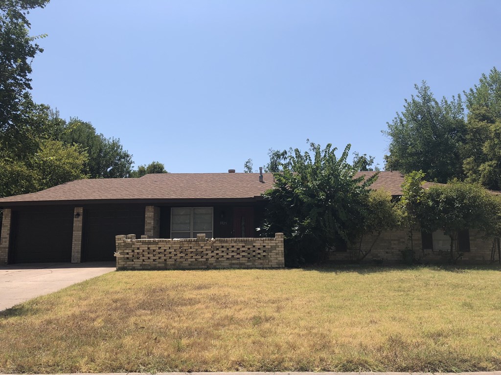 a house with a brick wall in front of a grass field