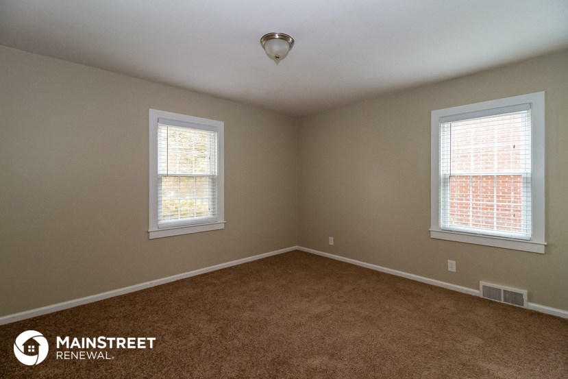 an empty room with two windows and a carpet