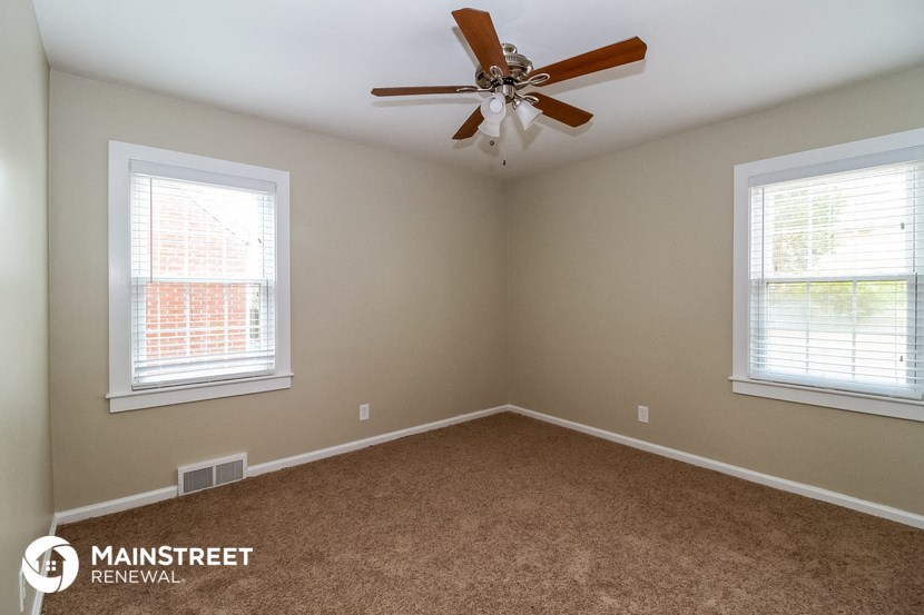 an empty room with a ceiling fan and two windows