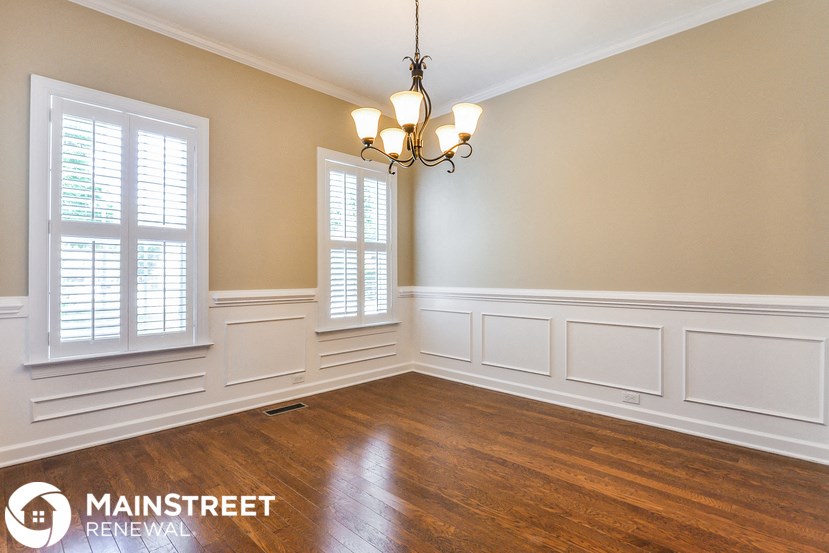 a dining room with white walls and wood floors and a chandelier