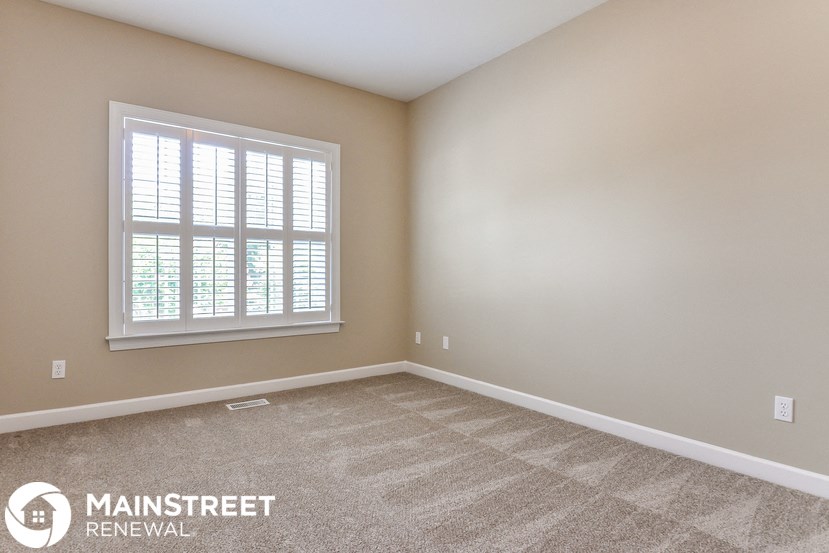 the living room of a new home with carpet and a window