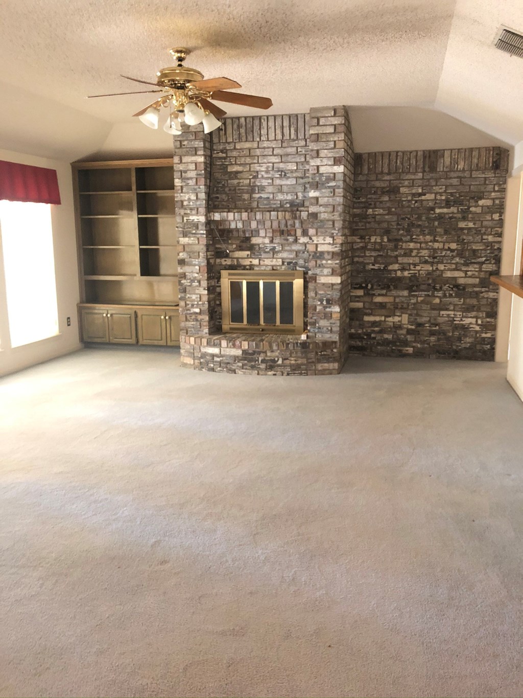 an empty living room with a fireplace and a ceiling fan