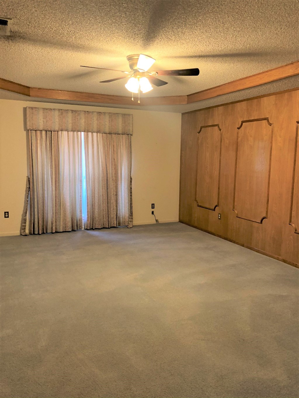 an empty living room with curtains and a ceiling fan