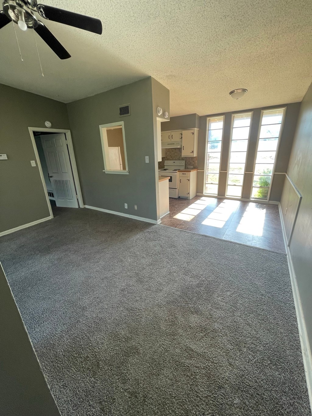 an empty living room with a kitchen in the background