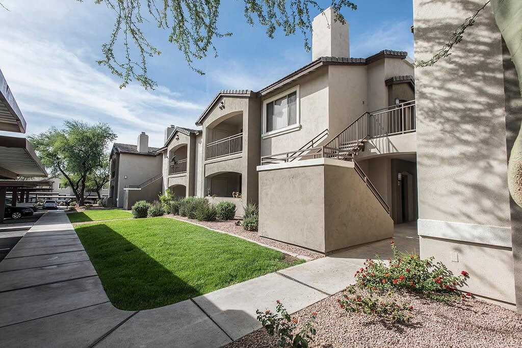 an exterior view of an apartment building with a yard and sidewalk