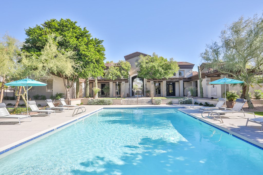 a swimming pool with chairs and umbrellas in front of a house
