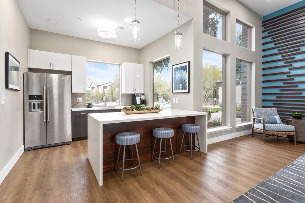 a kitchen with a large island with three stools and a stainless steel refrigerator
