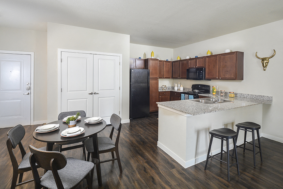 A kitchen with a table set for two and a black fridge.