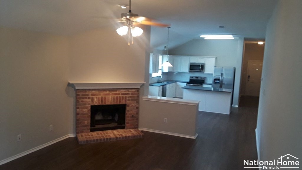 A living room with a fireplace and a kitchen in the background.