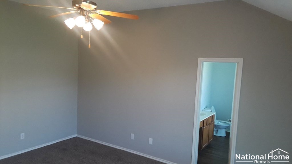 A room with a ceiling fan and a doorway leading to a bathroom.