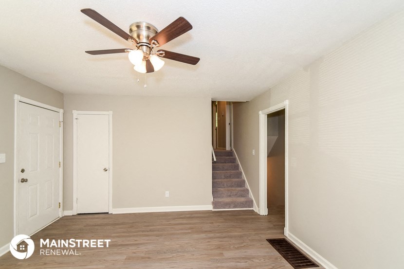 a living room with a ceiling fan and a door to a staircase