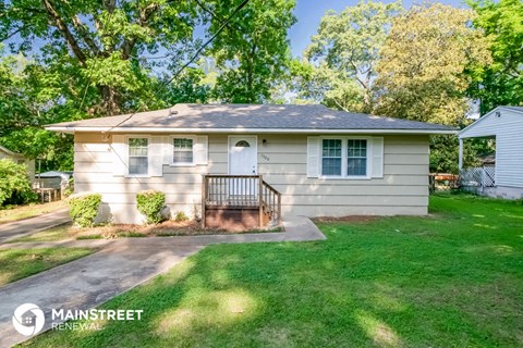 a small tan house with a front porch and a lawn