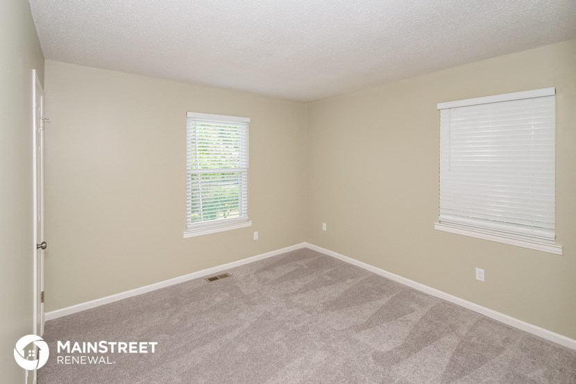 a bedroom with carpet and two windows