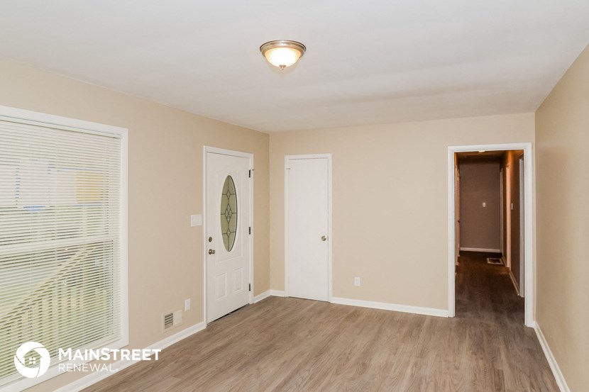 the living room of an apartment with a door to the hallway and a hallway mirror