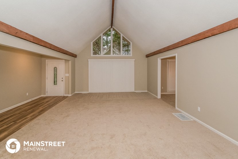 a spacious living room with a vaulted ceiling and a window