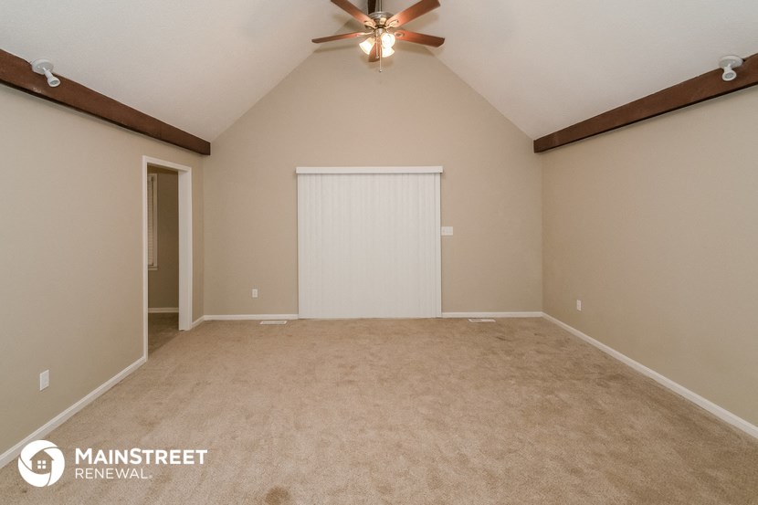 the spacious living room with ceiling fan and beige carpet