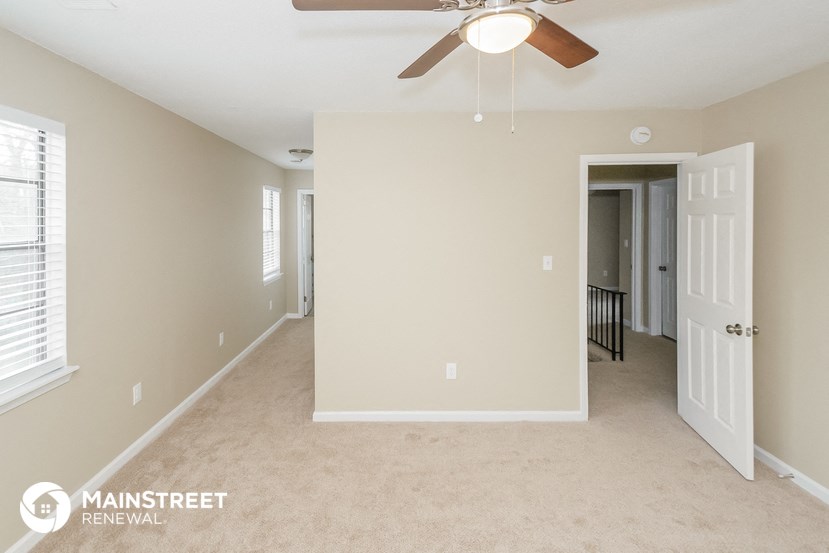 a living room with a ceiling fan and a hallway with a door to a bedroom