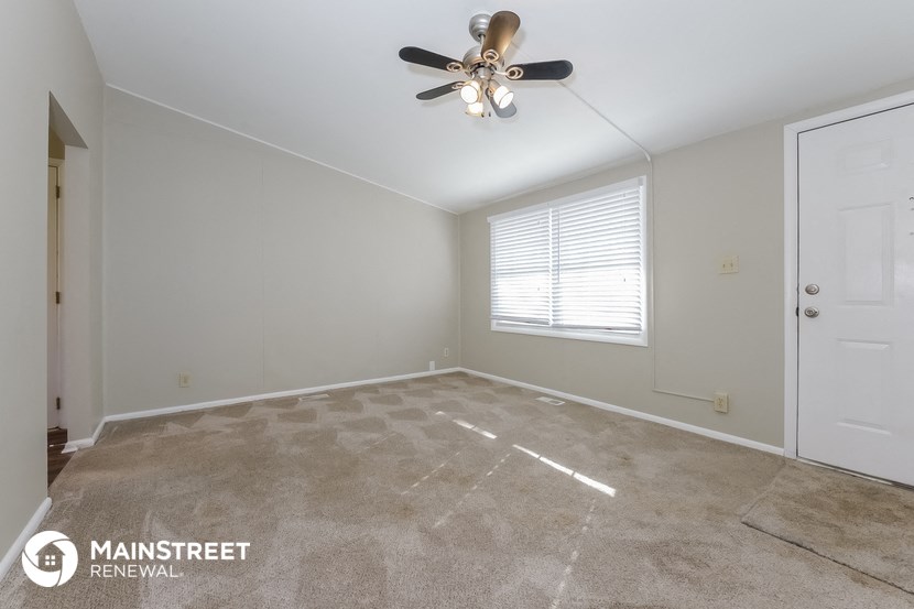 the living room of a home with a carpeted floor and a ceiling fan