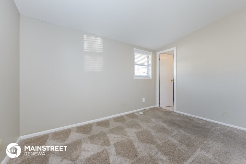 the spacious living room with carpeted flooring and white walls
