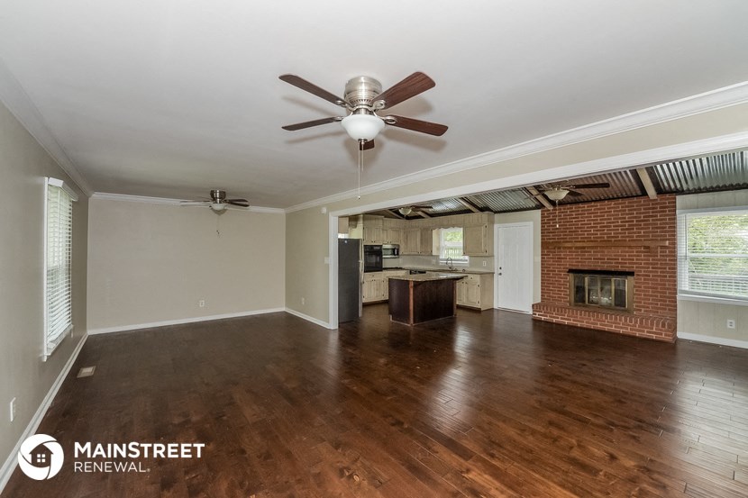 an empty living room with a brick fireplace and a ceiling fan