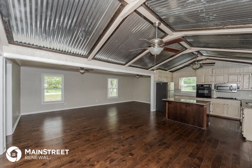 an empty living room with a kitchen and a ceiling fan
